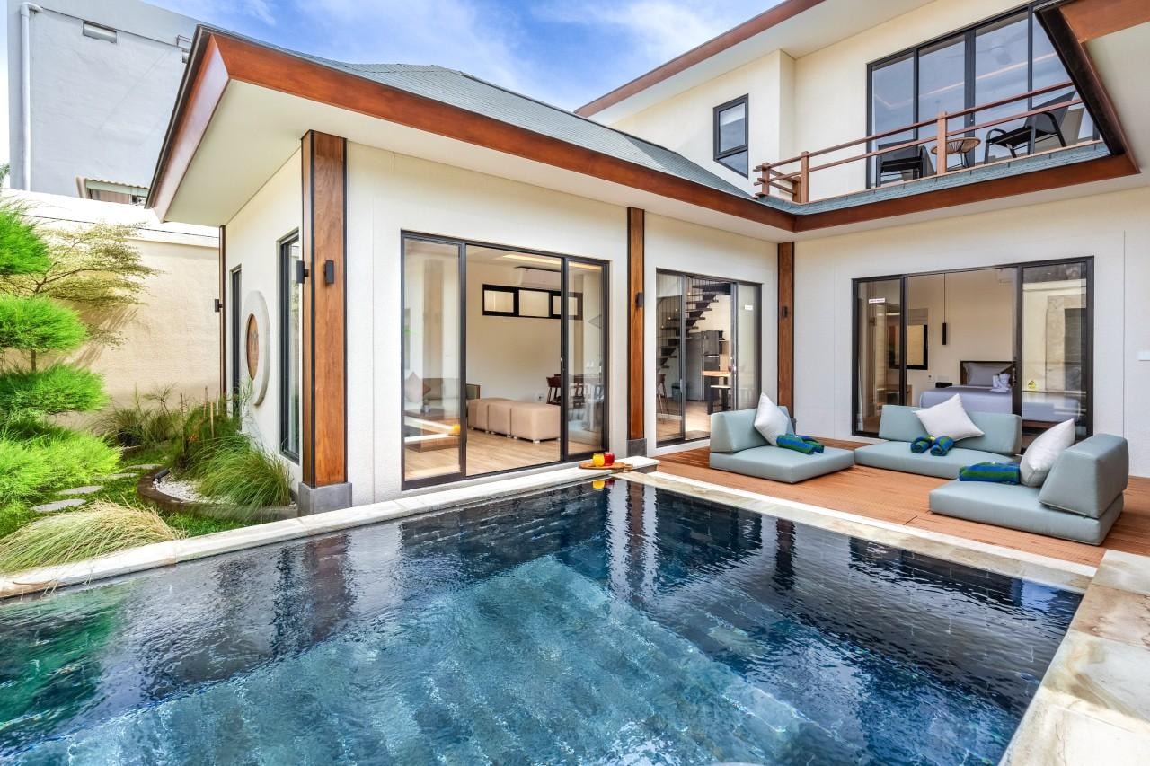 The villa and its pool in full daylight, seen across the water