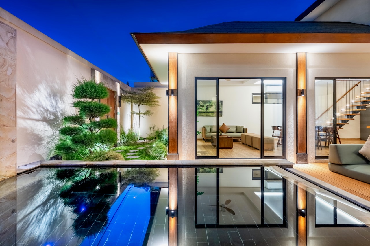 The lit villa and garden pine reflected in the private pool at blue hour