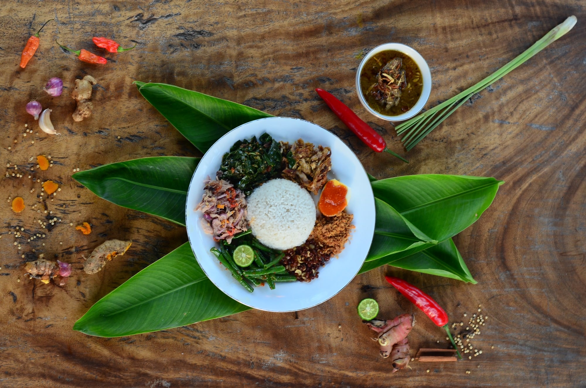 A plate of Balinese nasi campur on banana leaves, with sambal, chillies and spices on a wooden table